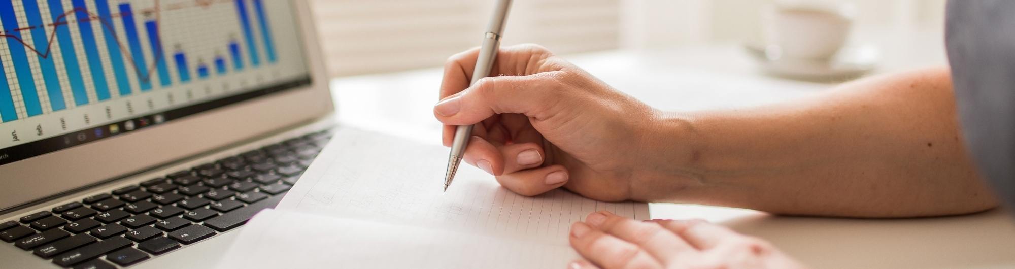 Personne qui prend des notes devant un ordinateur présentant des données